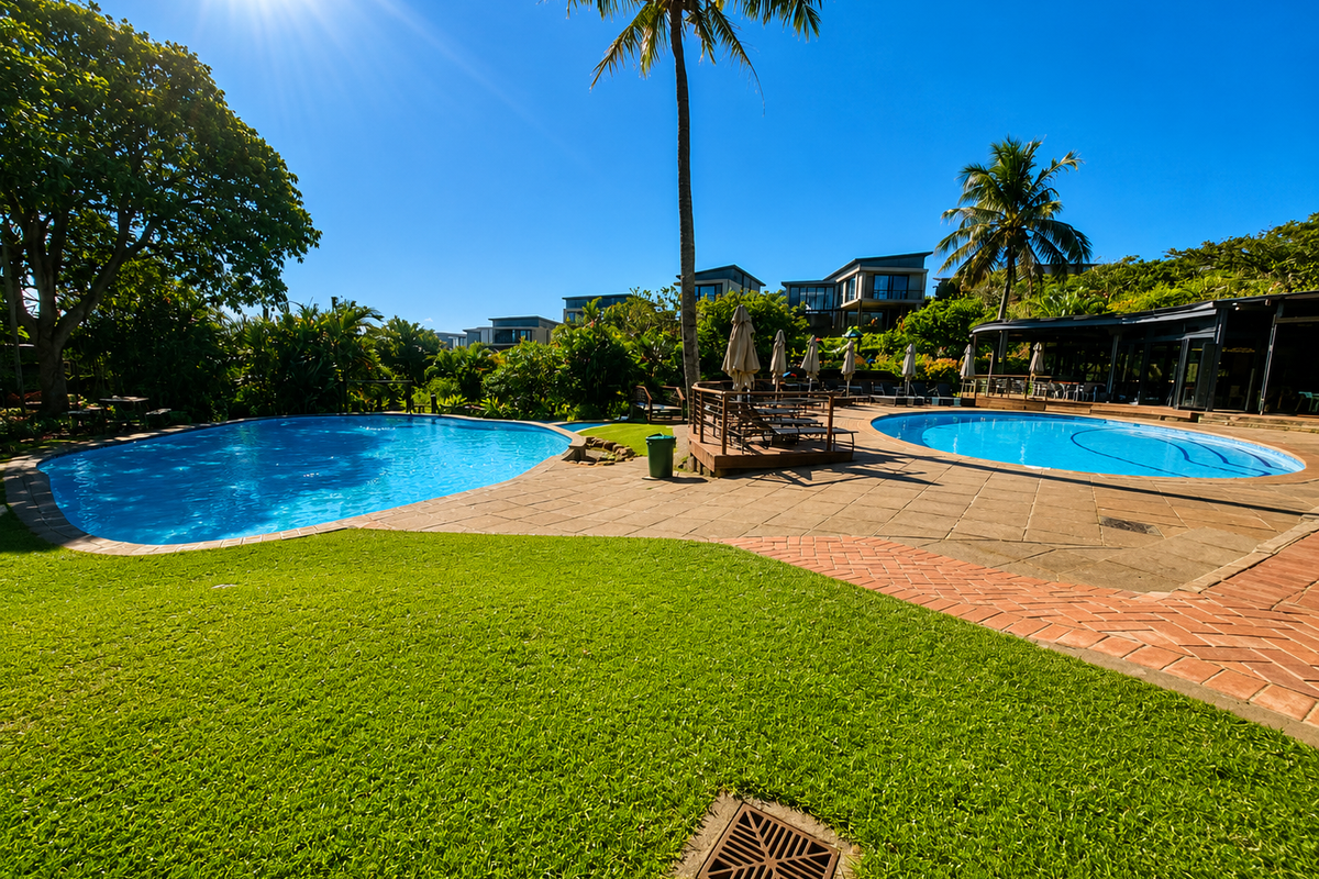 A well-maintained outdoor pool area featuring dual swimming pools, paved decking, and lush landscaped surroundings in a residential estate setting.