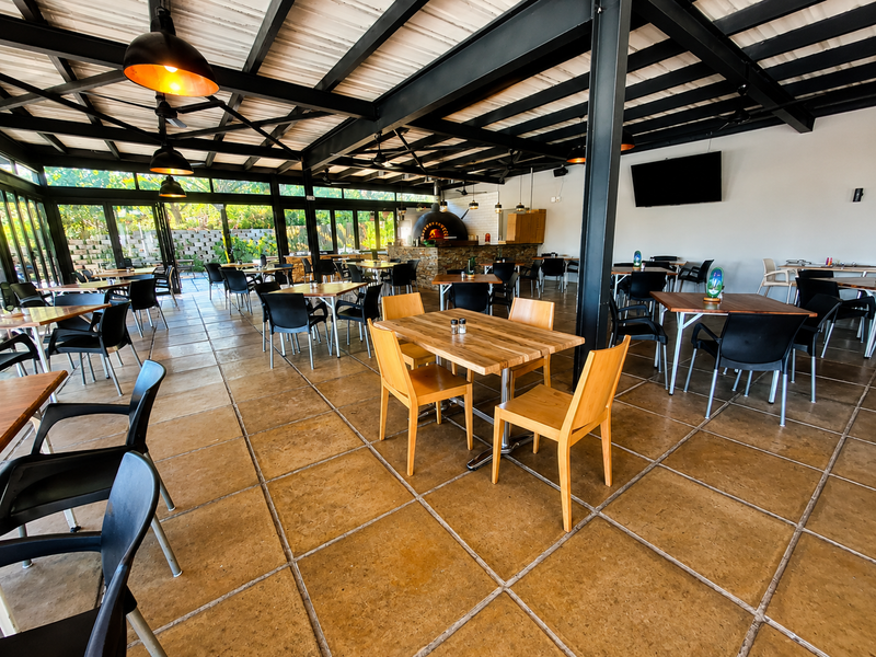 Spacious covered outdoor patio featuring exposed steel beams, tiled flooring, and a built-in stone pizza oven, ideal for large-scale entertaining.