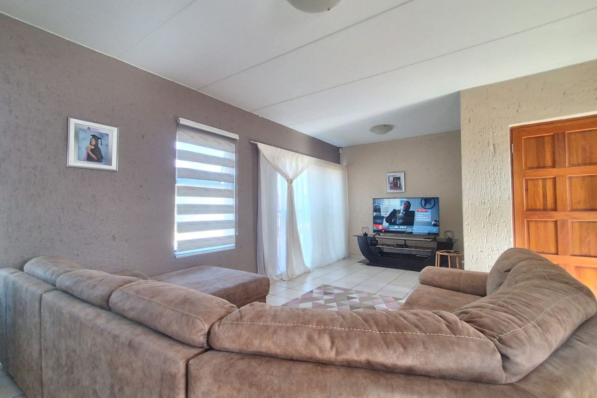 A comfortable living room featuring tiled flooring, a textured feature wall, and natural light through roller blinds and curtains.