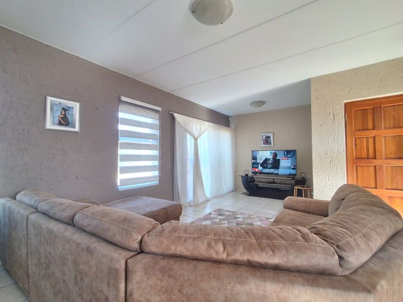 A comfortable living room featuring tiled flooring, a textured feature wall, and natural light through roller blinds and curtains.