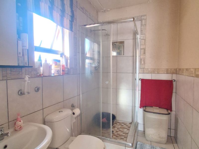 A functional bathroom featuring a shower enclosure, pedestal basin, and toilet, with tiled finishes. The space requires cosmetic updates and ceiling repairs.