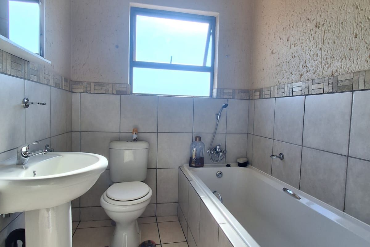 A functional bathroom featuring a pedestal basin, toilet, and a built-in bathtub with tiled walls and flooring.