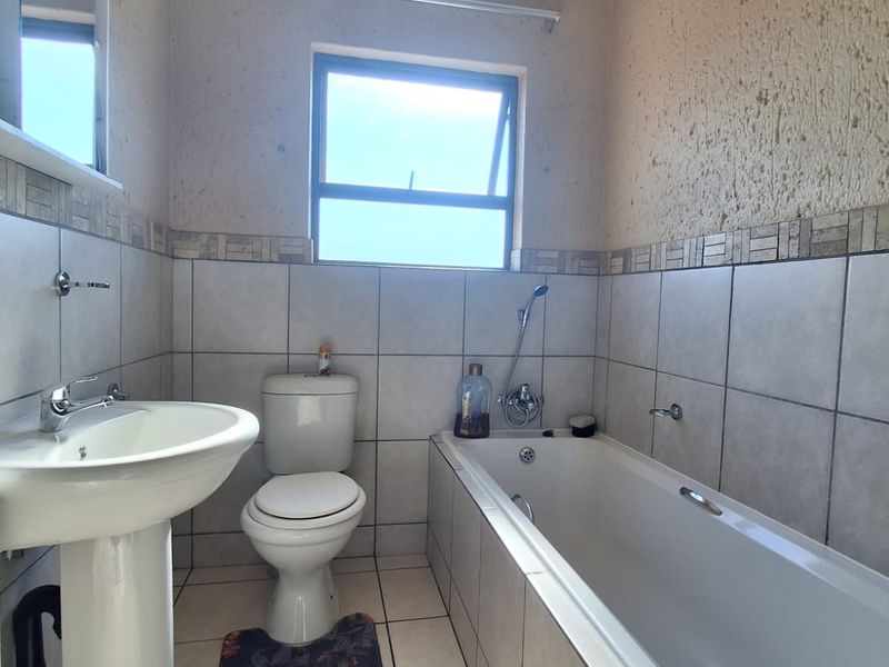 A functional bathroom featuring a pedestal basin, toilet, and a built-in bathtub with tiled walls and flooring.