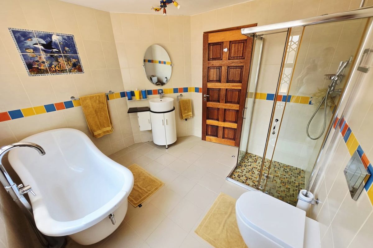 A functional bathroom featuring a freestanding bathtub, a separate glass-enclosed shower, a wall-mounted toilet, and a vanity basin with decorative tiled accents.