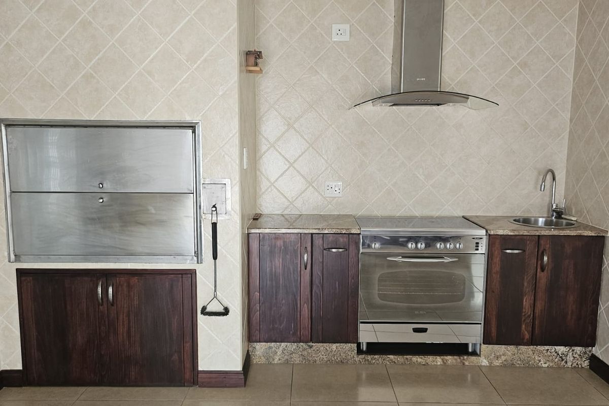 A functional kitchen area featuring dark wood cabinetry, granite countertops, a built-in stainless steel braai, and a stainless steel oven with extractor fan.