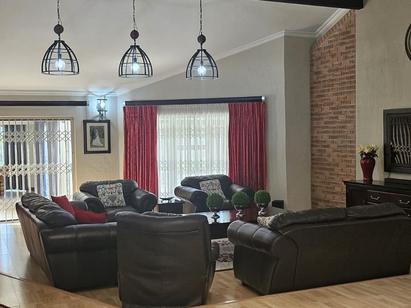 Spacious living room featuring a vaulted ceiling, exposed brick accent wall, laminate flooring, and pendant lighting, with direct access to an outdoor area.