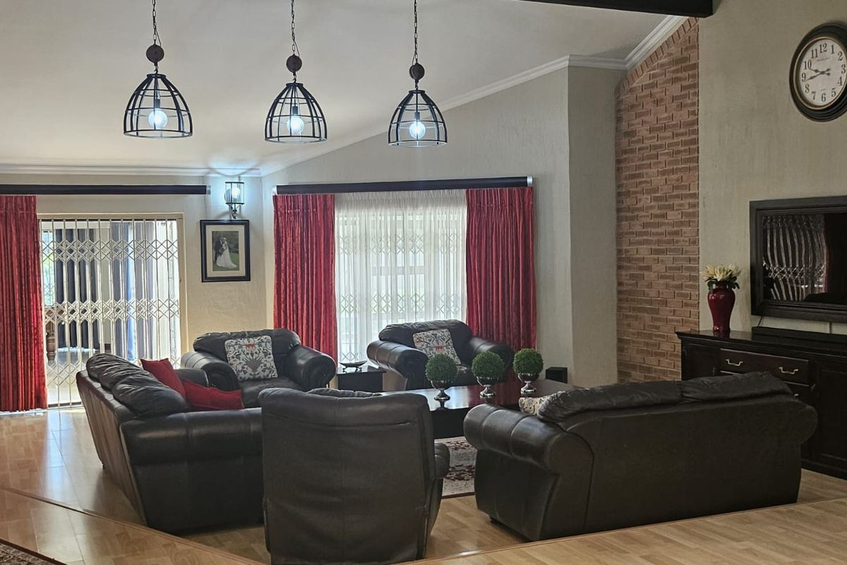 Spacious living room featuring a vaulted ceiling, exposed brick accent wall, laminate flooring, and pendant lighting, with direct access to an outdoor area.