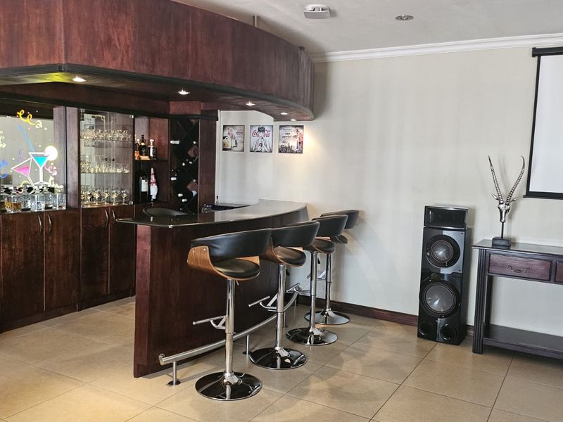 A well-appointed home bar area featuring custom dark wood cabinetry, integrated glass shelving, a curved bar counter, and recessed lighting.
