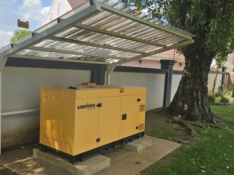 Outdoor utility area featuring a dedicated backup generator housed under a protective corrugated shelter on a concrete base.