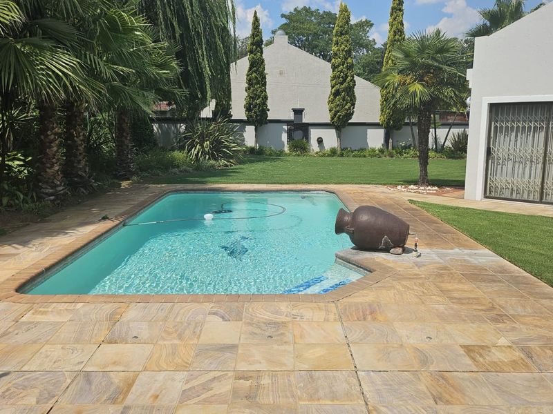 A well-maintained swimming pool area featuring stone paving, lush garden surroundings, and a secure entrance to the main dwelling.