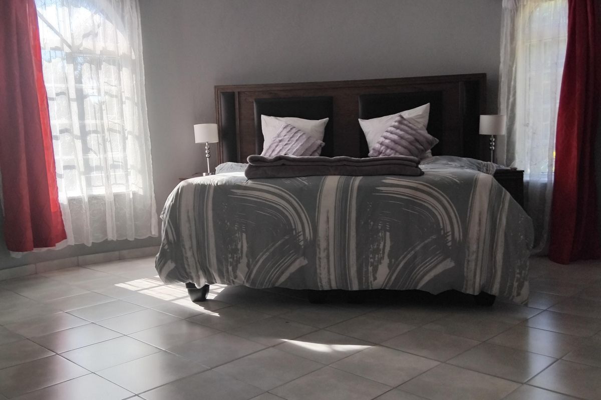 Spacious bedroom featuring a unique curved wall design, tiled flooring, and dual arched windows allowing for natural light.