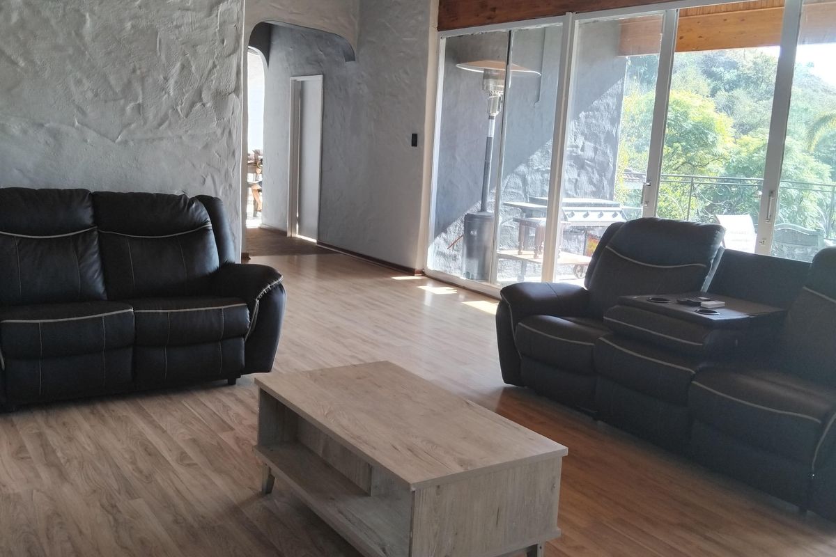 Spacious living room featuring exposed timber beam ceilings, textured plaster walls, laminate flooring, and large sliding glass doors providing natural light and outdoor access.