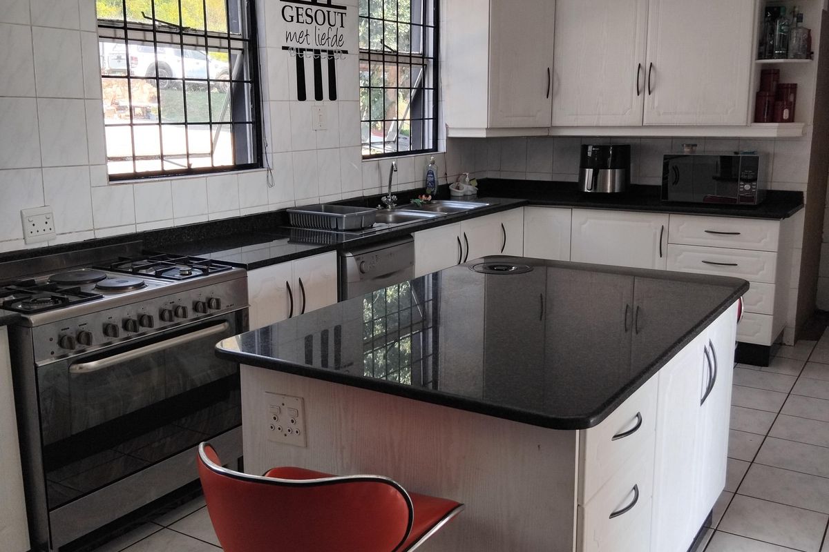 A functional kitchen featuring a central island with granite countertops, white cabinetry, gas stove, and tiled flooring with security bars on the windows.