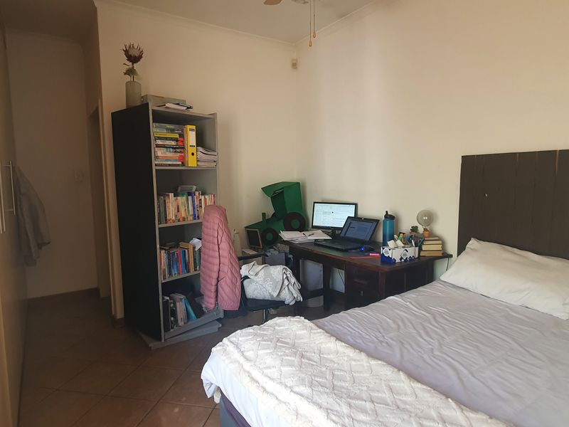 A functional bedroom featuring built-in cupboards, tiled flooring, and a ceiling fan, offering a practical layout for comfortable living.
