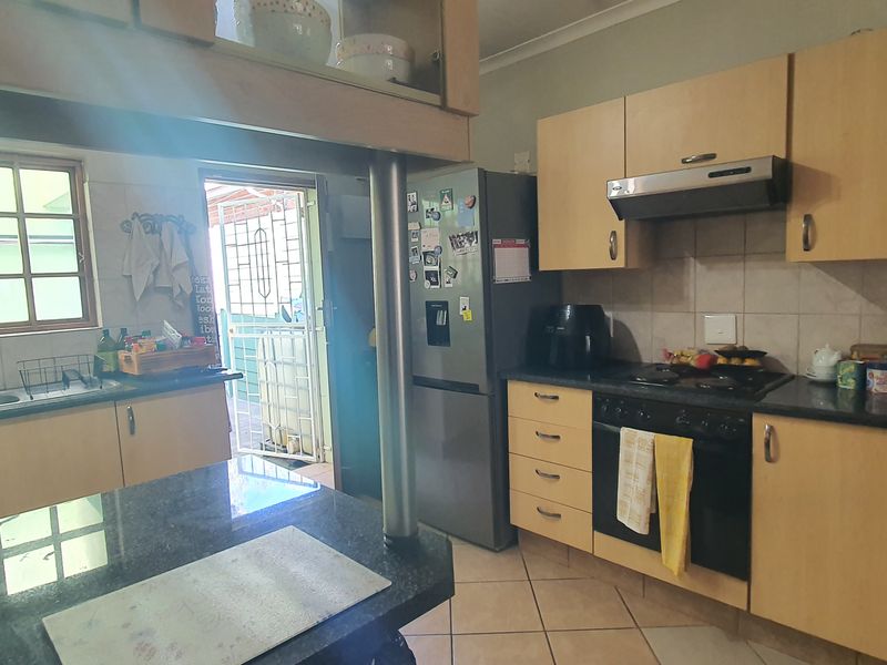 Functional kitchen featuring laminate cabinetry, granite countertops, built-in oven with hob, extractor fan, and tiled flooring with direct access to an exterior area.