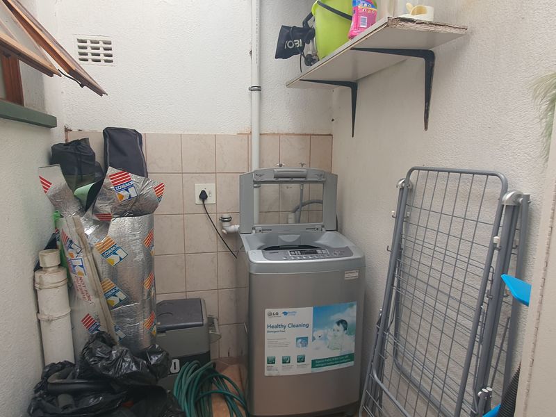 A compact laundry area featuring tiled splashback, wall-mounted shelving, and dedicated plumbing connections for a washing machine.