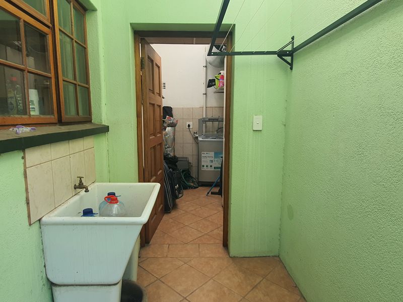 A functional laundry area featuring a ceramic utility sink, tiled flooring, and a wall-mounted drying rack, providing a practical space for household chores.