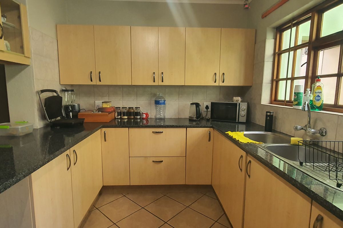 A functional kitchen featuring light wood-finish cabinetry, granite countertops, a double stainless steel sink, and tiled flooring with natural light from the window.