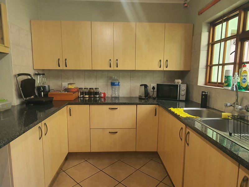 A functional kitchen featuring light wood-finish cabinetry, granite countertops, a double stainless steel sink, and tiled flooring with natural light from the window.