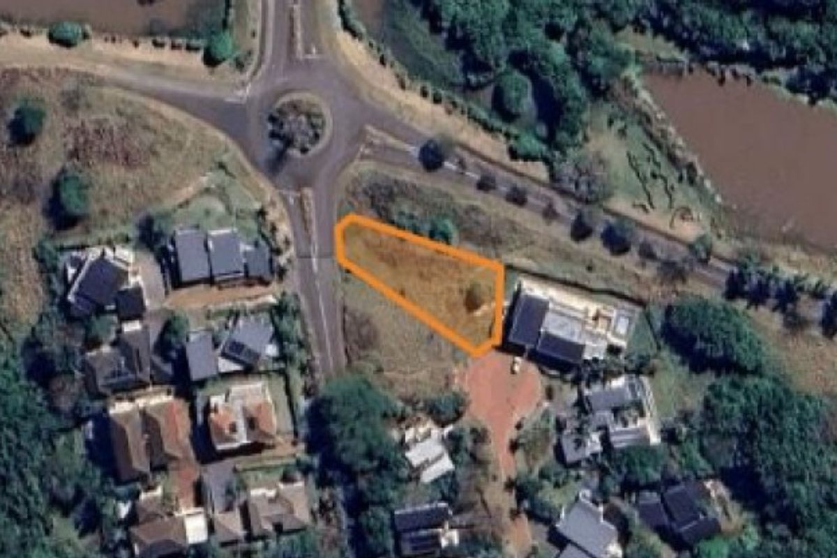 Aerial view of a vacant residential plot highlighted in orange, situated within a developed neighborhood near a roundabout and water feature.