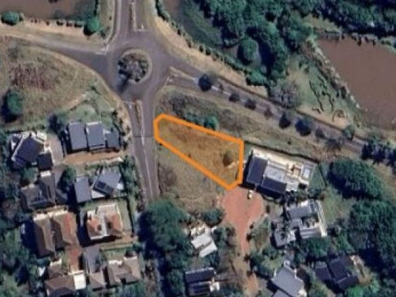 Aerial view of a vacant residential plot highlighted in orange, situated within a developed neighborhood near a roundabout and water feature.