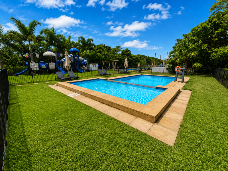 Well-maintained outdoor swimming pool area featuring stone coping, surrounding lawn, and secure metal perimeter fencing in a landscaped setting.