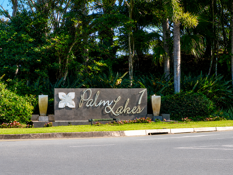 A well-maintained entrance sign for Palm Lakes estate, featuring professional landscaping and clear street-level visibility.