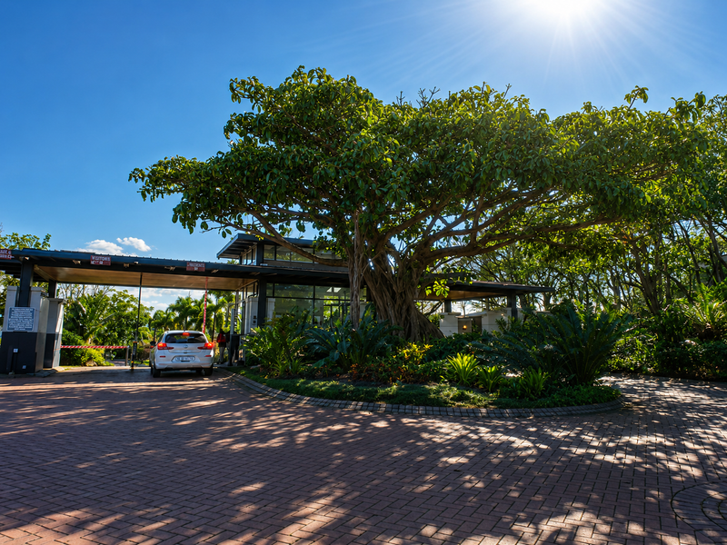 A well-maintained residential estate entrance featuring a modern security gatehouse, paved driveway, and mature landscaped gardens.