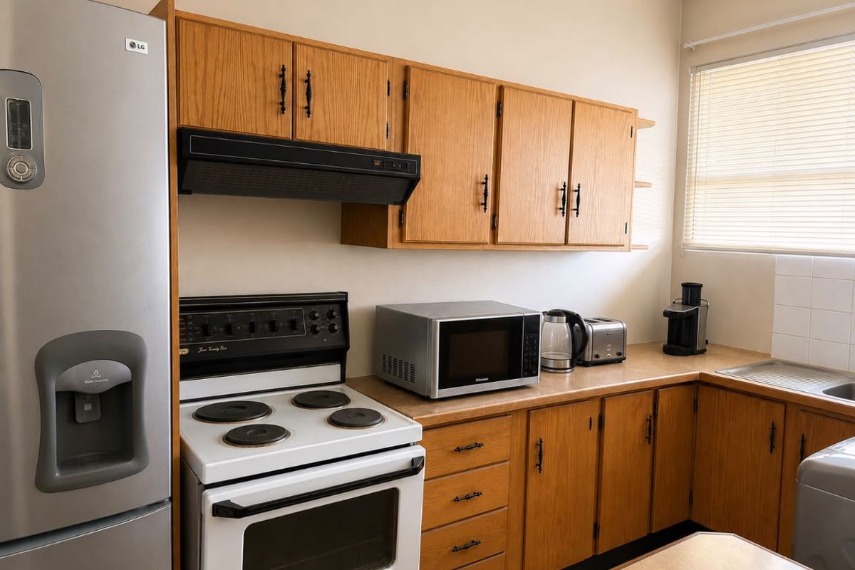A functional kitchen featuring wooden cabinetry, an electric stove with an extractor fan, and a stainless steel sink with natural light from the window.