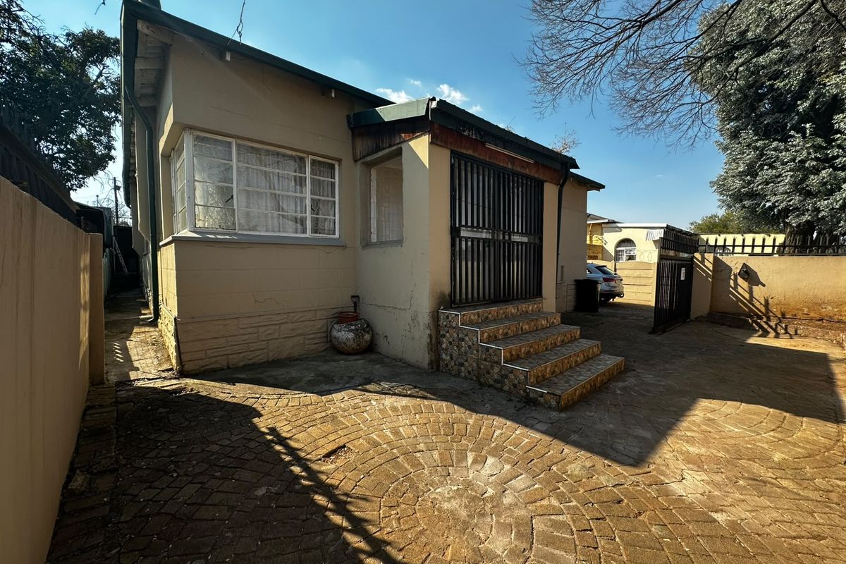 Rear exterior view of the property featuring a paved courtyard, security gate, and tiled entrance steps leading to the main structure.