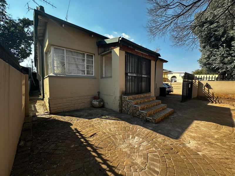 Rear exterior view of the property featuring a paved courtyard, security gate, and tiled entrance steps leading to the main structure.