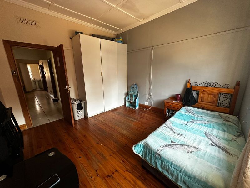 A bedroom featuring original timber flooring, built-in wardrobe storage, and a classic ceiling tile finish, offering a functional space with potential for cosmetic updates.