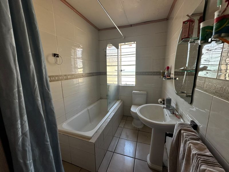 A functional bathroom featuring a bathtub with a glass screen, pedestal basin, and toilet, finished with tiled walls and flooring.