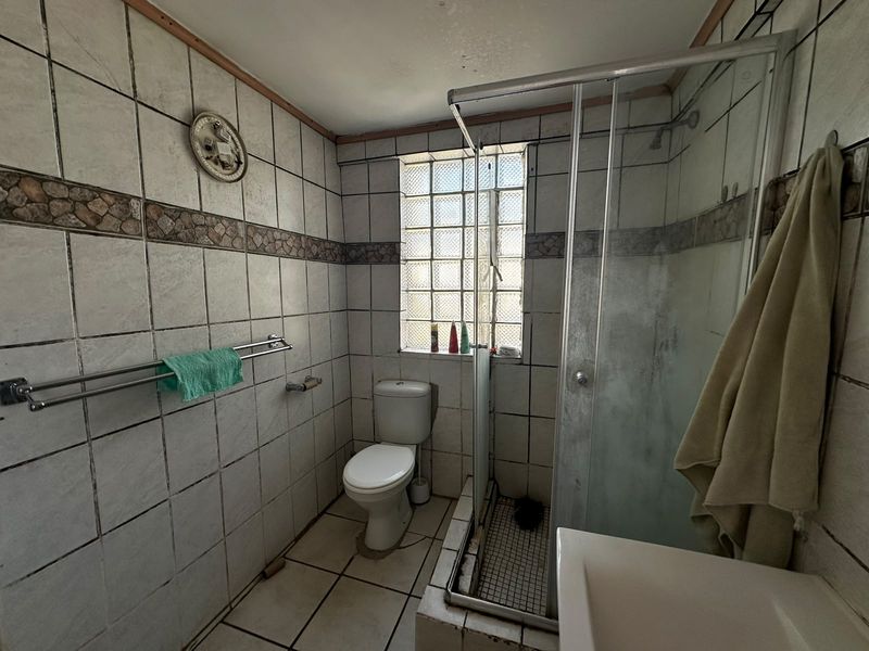 A dated bathroom featuring a shower enclosure, toilet, and glass block window, requiring modernization of finishes and fixtures.