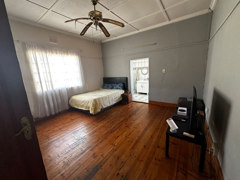 Spacious bedroom featuring original timber flooring, a ceiling fan, and an adjoining ensuite bathroom with tiled finishes.