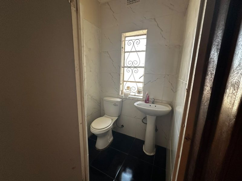 A compact guest bathroom featuring a pedestal basin, toilet, and tiled finishes, requiring minor cosmetic updates.