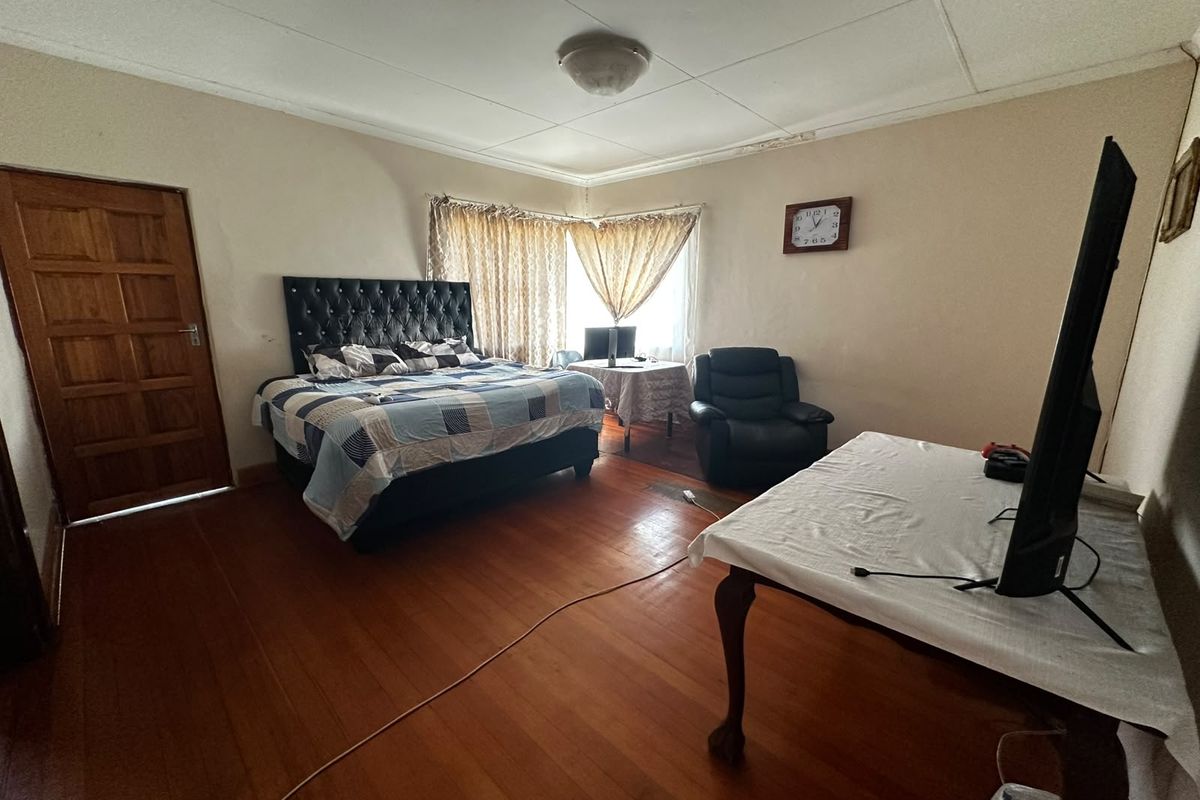 Spacious bedroom featuring warm timber flooring and a classic panelled timber door, requiring some cosmetic attention to the ceiling finishes.