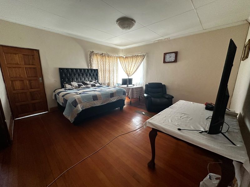 Spacious bedroom featuring warm timber flooring and a classic panelled timber door, requiring some cosmetic attention to the ceiling finishes.