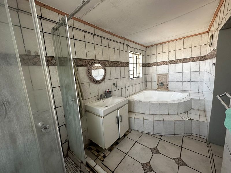 A dated bathroom featuring a built-in corner bathtub, a separate glass shower enclosure, and a vanity unit, requiring cosmetic updates to modernize the space.