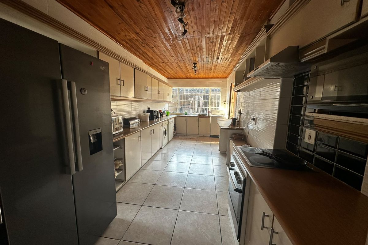A functional galley-style kitchen featuring tiled flooring, timber ceiling, built-in cabinetry, and integrated cooking appliances.