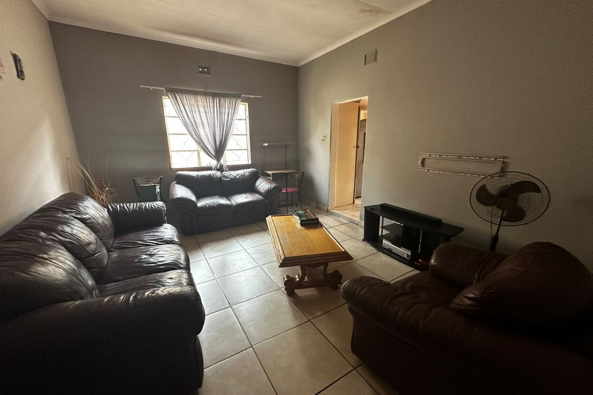 A living room featuring tiled flooring and coved ceilings, showing signs of wear including ceiling water staining and wall paint damage.