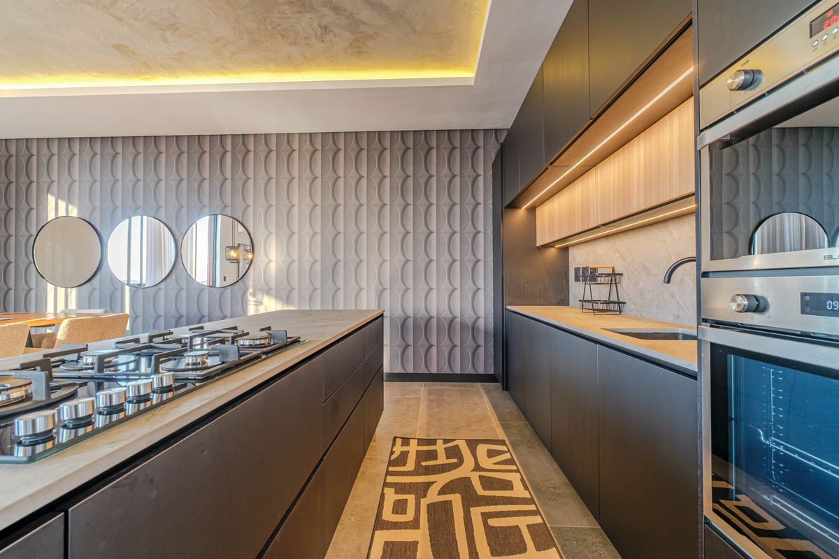 Modern, high-end kitchen featuring dark cabinetry, stone countertops, a gas cooktop island, built-in oven, and sophisticated recessed lighting.