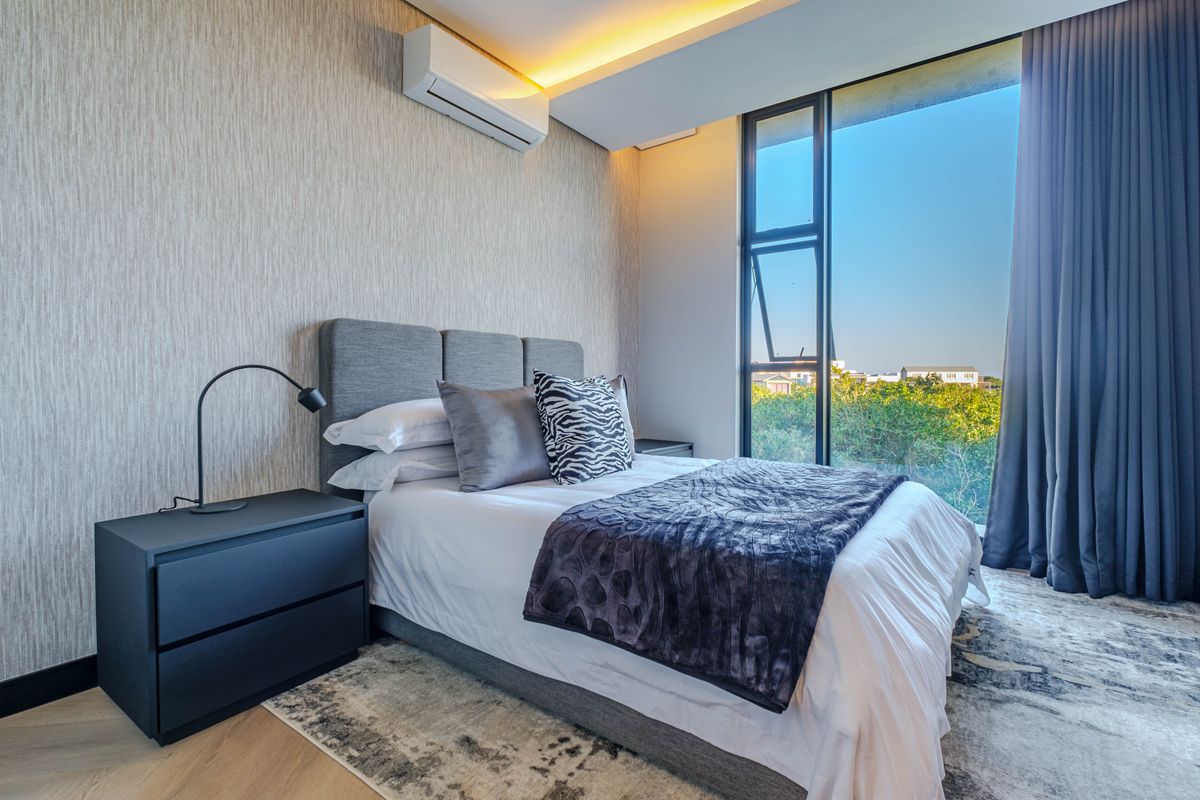 Modern bedroom featuring textured wallpaper, recessed ceiling lighting, split-system air conditioning, and large windows with natural light and exterior views.