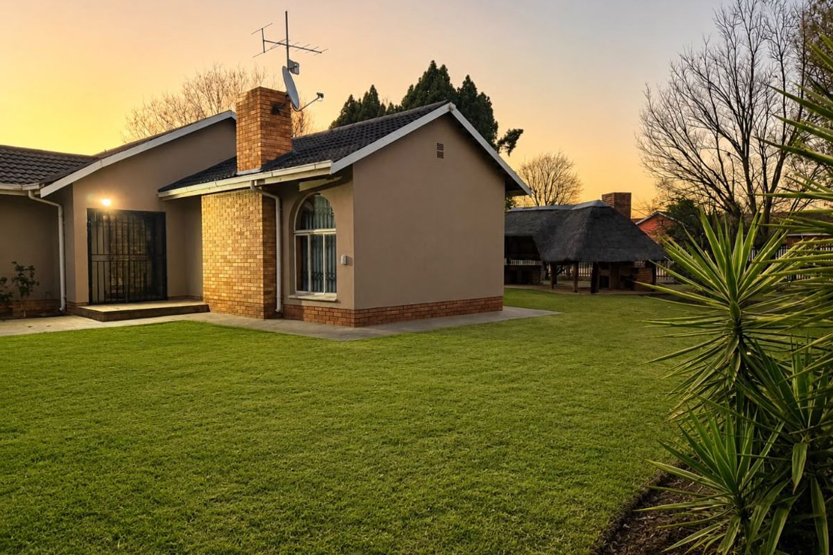 A well-maintained rear garden featuring a brick chimney, arched window, and a separate thatched lapa area under a sunset sky.
