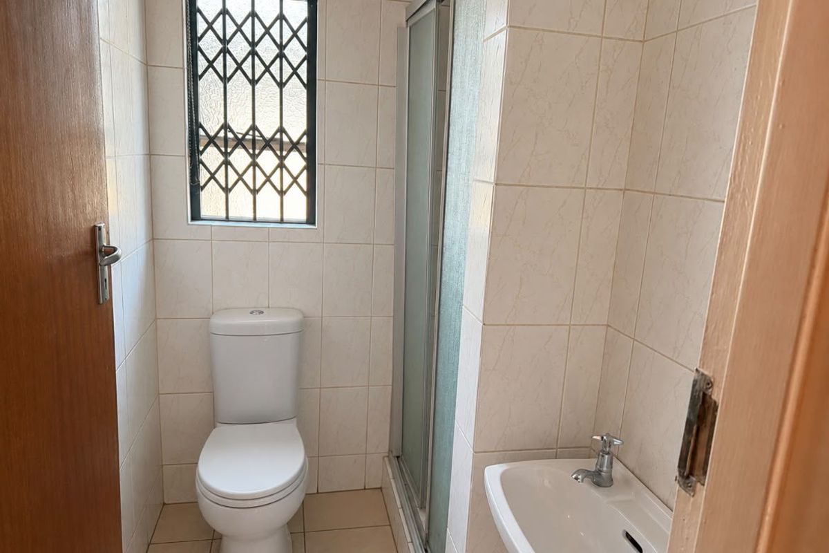 A compact bathroom featuring a shower enclosure, toilet, and wall-mounted washbasin with neutral wall and floor tiling.