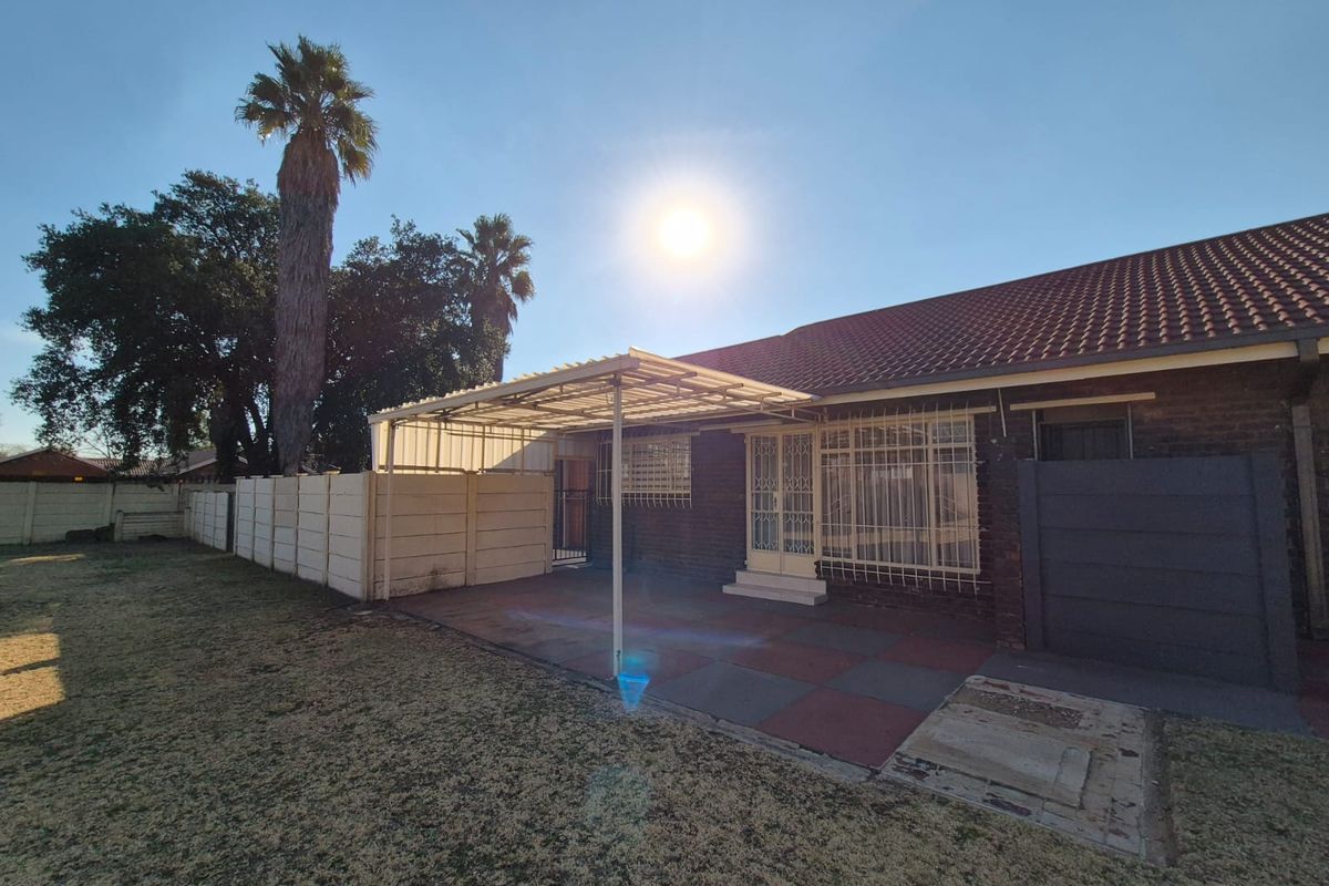 Rear view of the property featuring a covered patio area, brick exterior, security features, and a large garden with precast boundary walls.