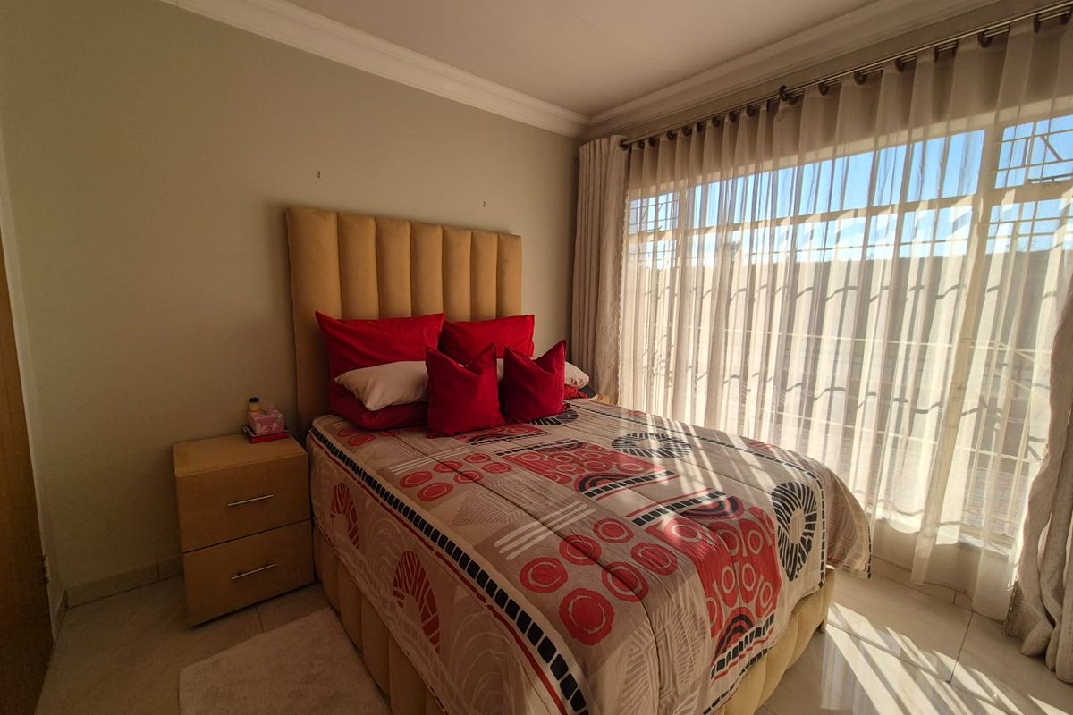 A well-lit bedroom featuring tiled flooring, decorative cornice, and large windows with fitted curtain tracks and security bars.