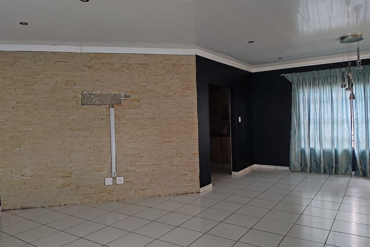 Spacious living area featuring a stone veneer accent wall, tiled flooring, and recessed lighting, presenting a blank canvas for interior design.