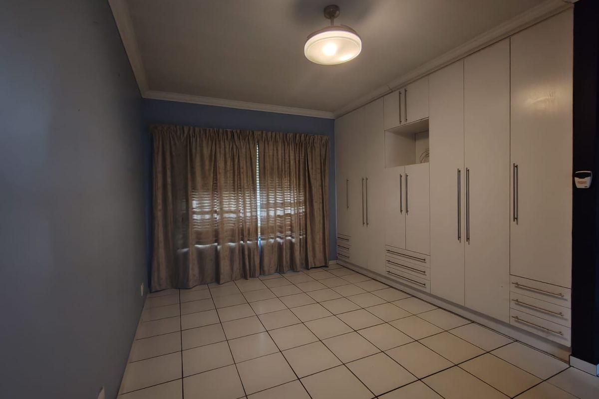 A spacious, empty bedroom featuring extensive built-in white cabinetry, tiled flooring, and neutral wall tones, offering a clean canvas for personalization.