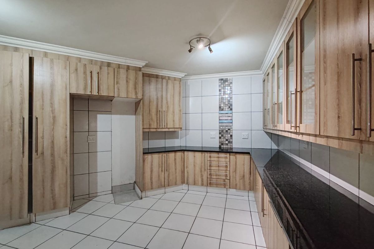 A clean, empty kitchen featuring light wood-look cabinetry, dark granite countertops, and white tiled flooring with a decorative mosaic backsplash accent.